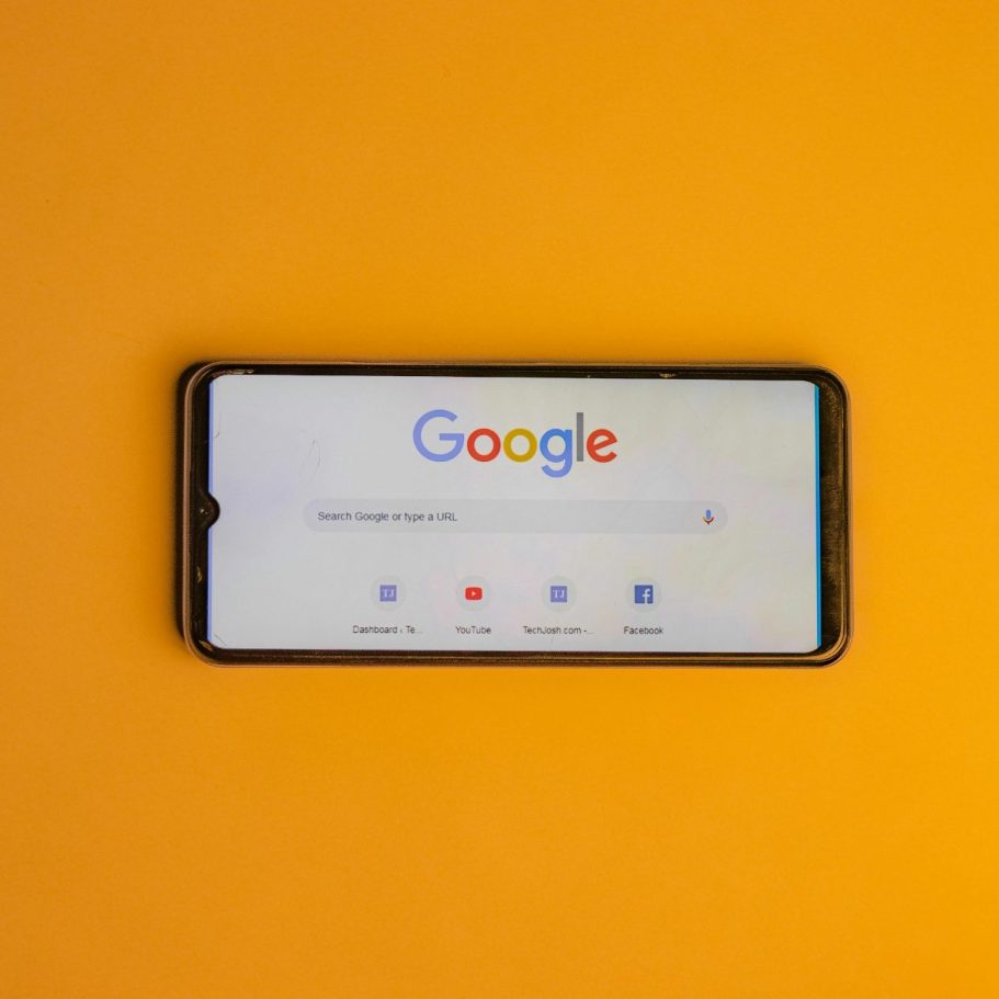 Smartphone mit geöffneter Google-Suchseite auf orangefarbenem Hintergrund.
