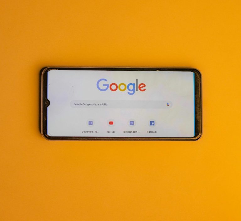 Smartphone mit Google-Suchseite auf orangefarbenem Hintergrund.