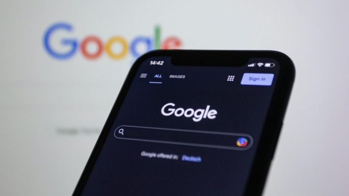 Smartphone zeigt die Google-Startseite im Dunkelmodus. Suchfeld ist aktiv.
